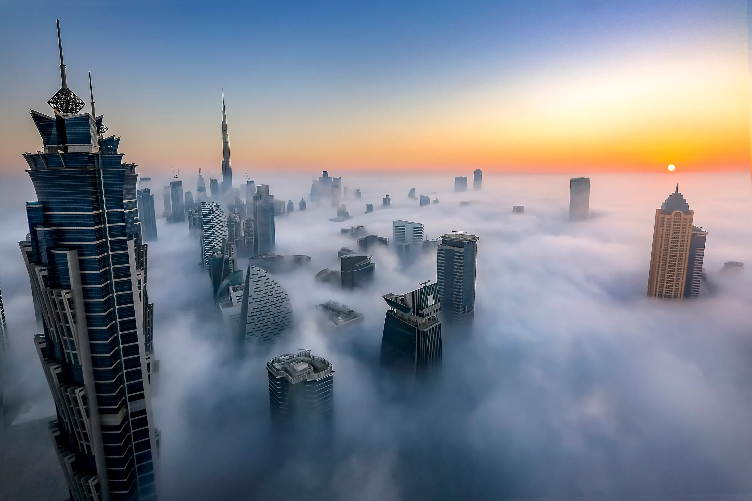 Dubai at sunrise under thick fog. Only the tallest towers stand clear of it.