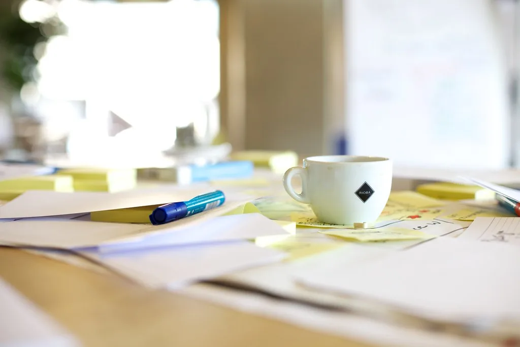 A workshop table covered in sticky notes and paper, a pen and a coffee cup among them.